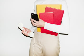 a person holding a wire phone, telephone and notebooks, body cropped from neck to thighs