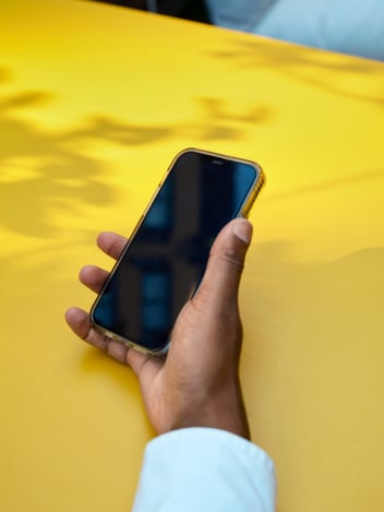 Person holding a iphone, hand on a yellow table