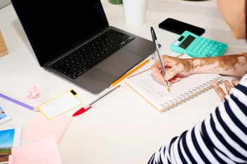 Person writing to notebook in front of laptop