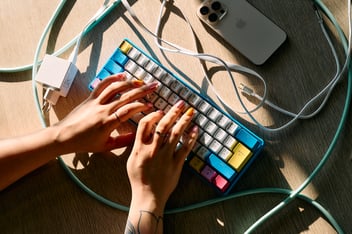 Hands with colorful fingernails on a blue-yellow-pink-white keyboard with cords around the keyboard