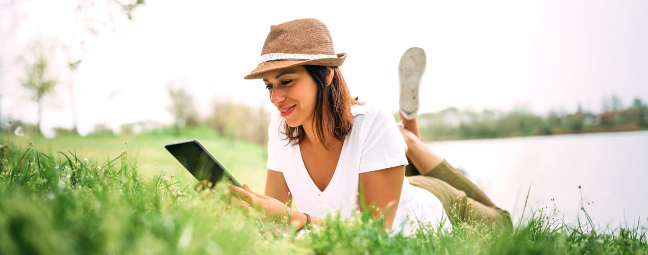 Person lying in grass reading a tablet