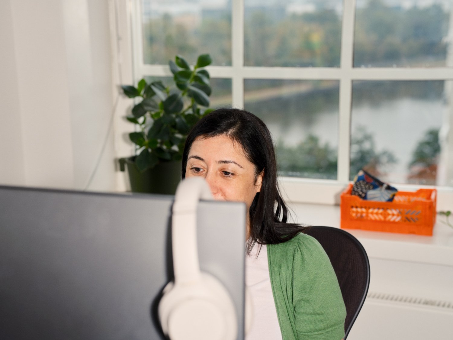 A woman behind a desktop screen with her face partially hidden by the screen.