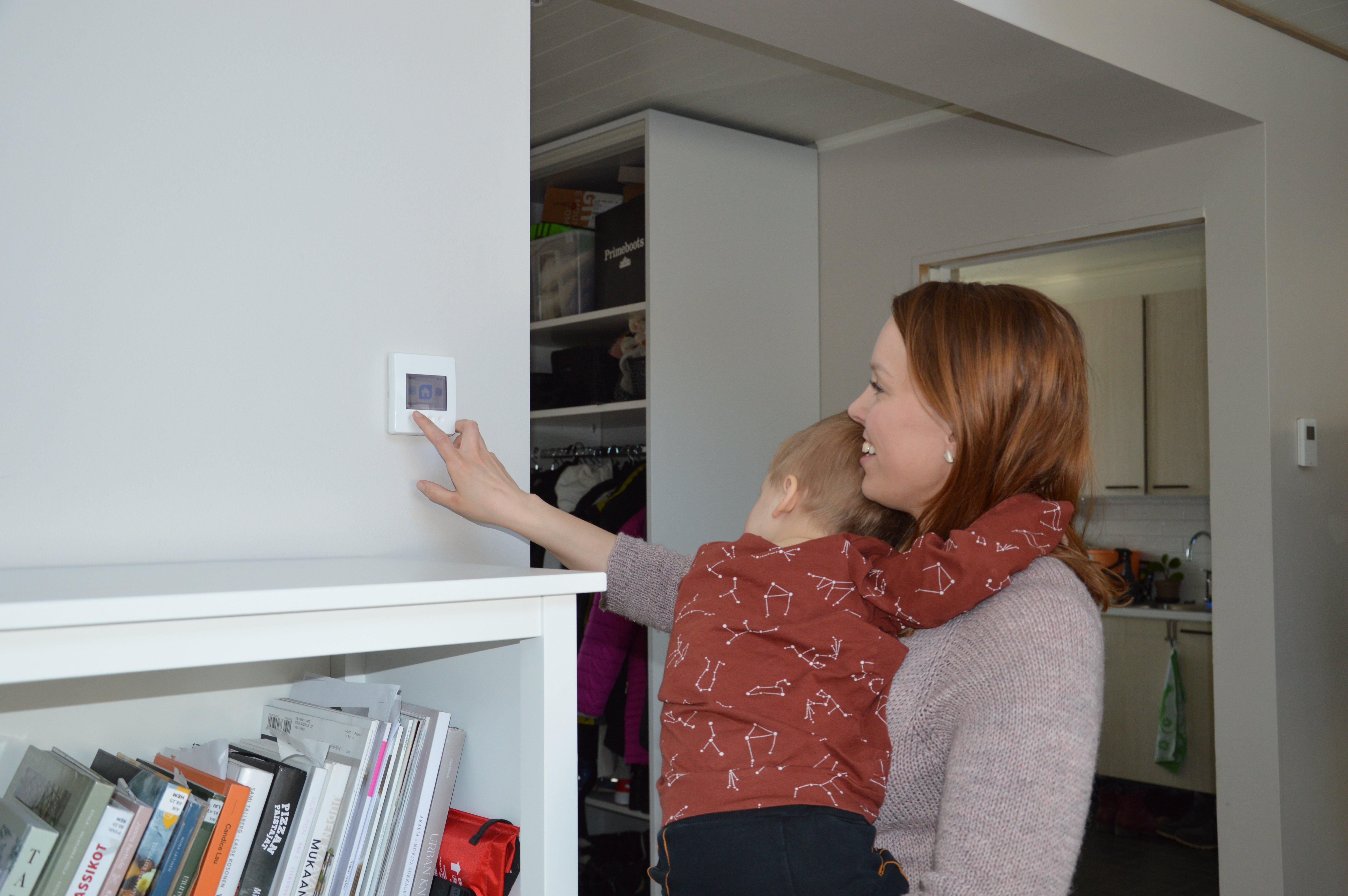 A lady with a kid on her lap operating a Vallox ventilation system.