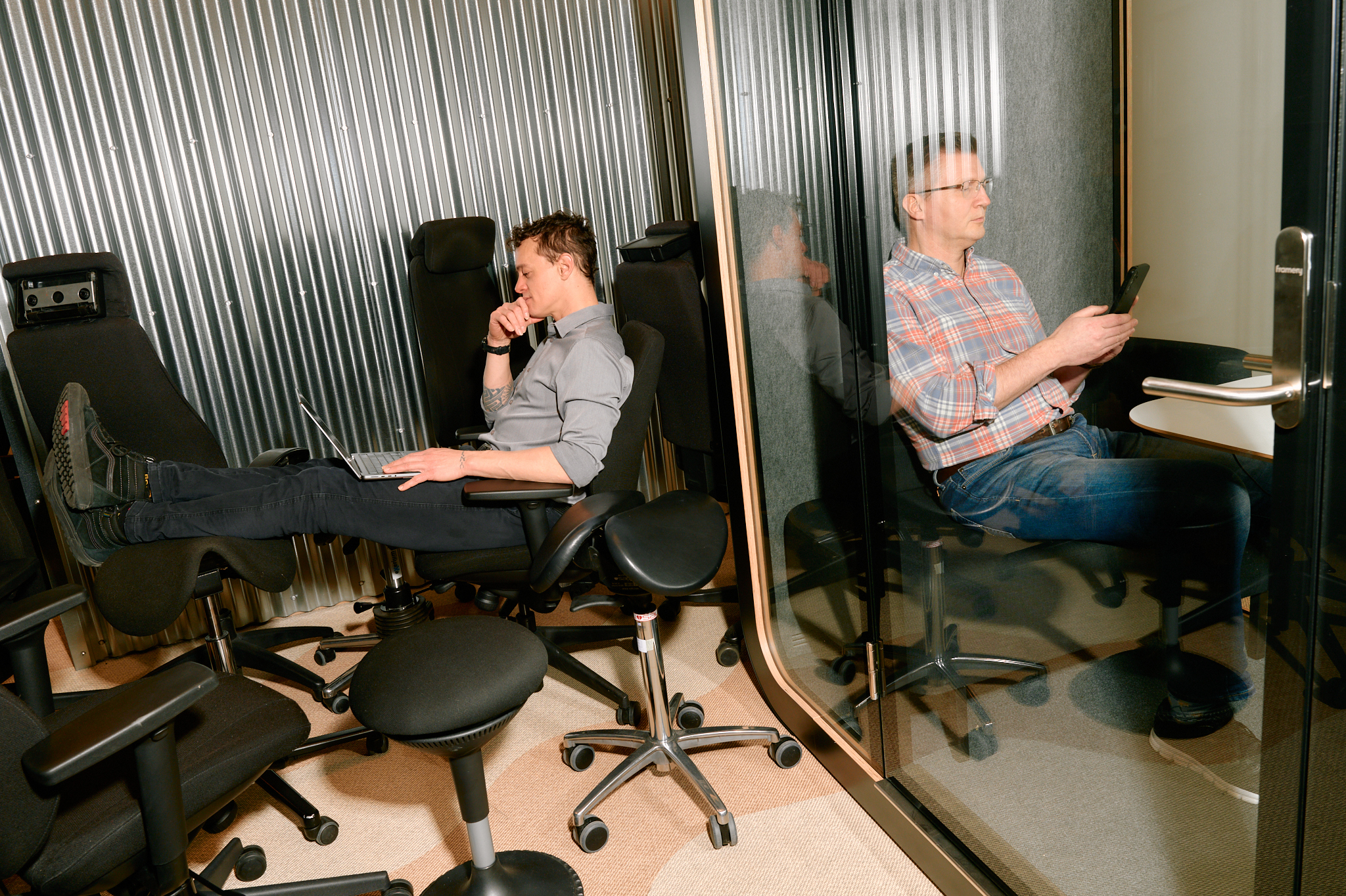 Two colleagues working in an office with ergonomic chairs and a glass meeting pod