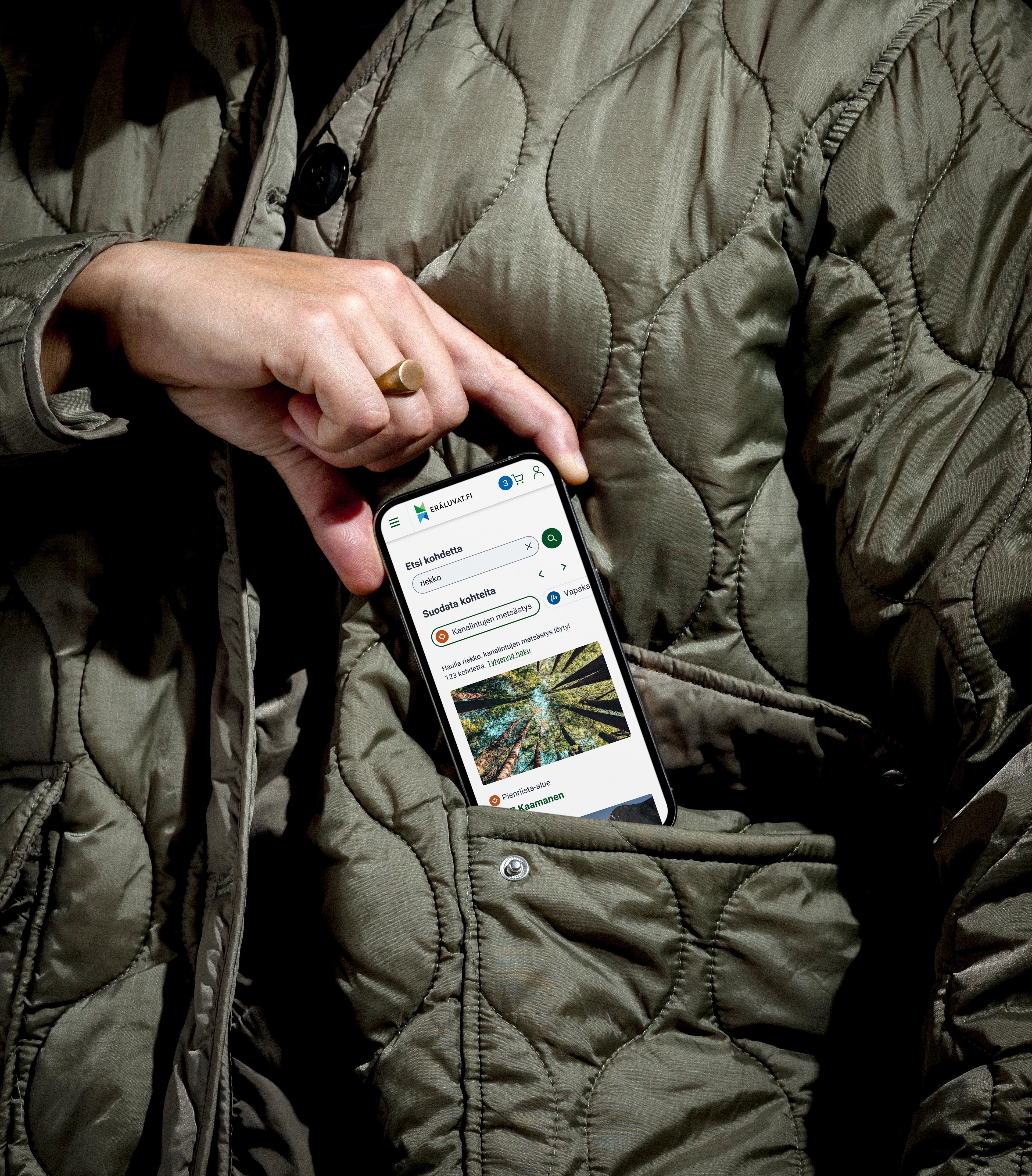 Eräluvat.fi mobile UI on a mobile phone held by a hand over a chest pocket