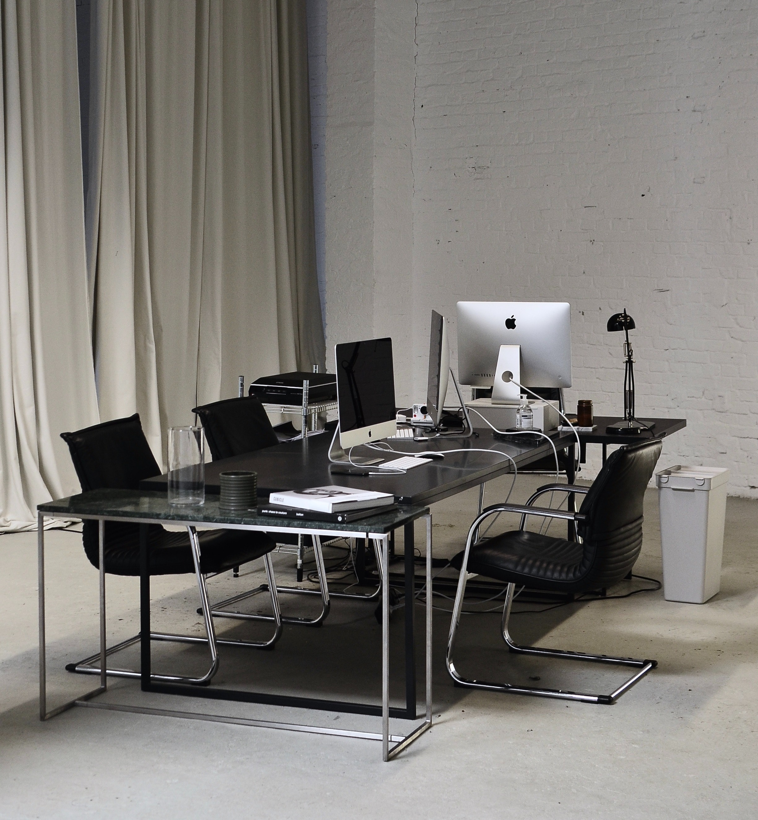 an industrial office space with a black table, black chairs and two apple computers